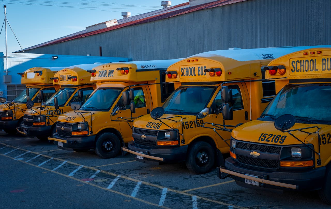 A line of yellow school buses parked outside a building during the day.